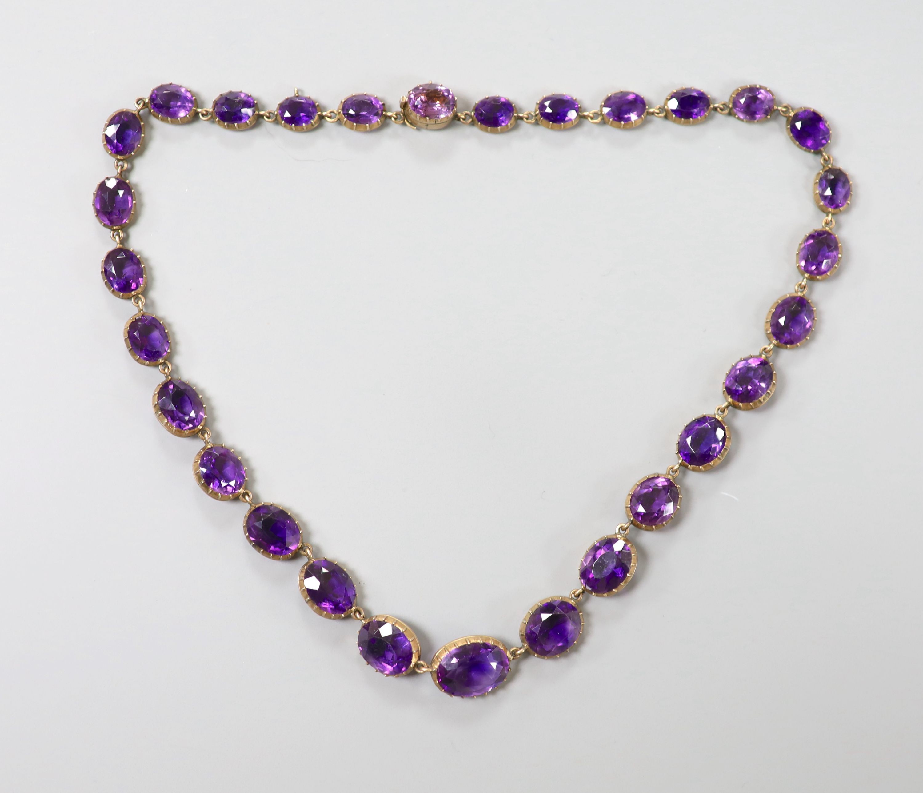 A late Victorian yellow metal and graduated oval cut amethyst set riviere necklace, 39cm, gross weight 37 grams.